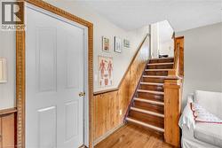 Hardwood flooring, wood-paneled wall, wood staircase with ornate newel post, white panel door, and decorative door trim - 