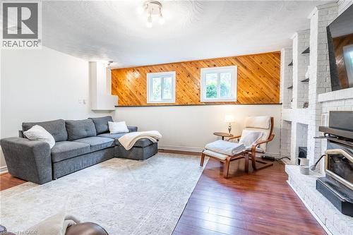 Warm wood-finish flooring, white painted brick fireplace with built-in shelving, two windows for natural light, and wood paneling accent wall - 152 Concession 7 Road E, Millgrove, ON - Indoor Photo Showing Living Room With Fireplace