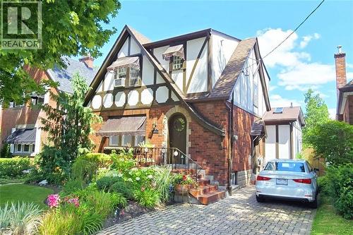 Tudor Revival architectural style featuring brick and half-timbering, a front entry archway, decorative window awnings, and an interlocking brick driveway - 107 Bond Street S, Hamilton, ON - Outdoor
