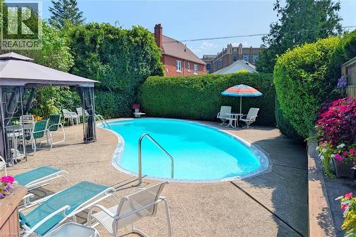 Freeform swimming pool with a concrete surround, privacy hedging, and built-in entry steps - 107 Bond Street S, Hamilton, ON - Outdoor With In Ground Pool With Backyard