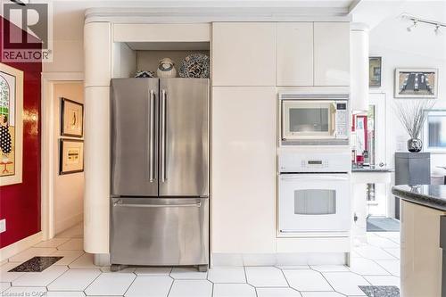 Stainless steel refrigerator, built-in microwave, integrated wall oven, white hexagonal floor tiling, and cream-colored cabinetry - 107 Bond Street S, Hamilton, ON - Indoor Photo Showing Kitchen