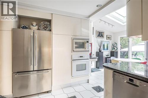 Kitchen featuring stainless steel refrigerator, integrated microwave and oven, built-in dishwasher, black granite-style countertops, and white hexagon tile flooring with dark accent tiles - 107 Bond Street S, Hamilton, ON - Indoor Photo Showing Kitchen