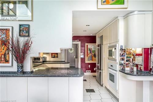 Built-in stainless steel appliances, granite-look countertops, white cabinetry with integrated handles, and hexagonal floor tiling - 107 Bond Street S, Hamilton, ON - Indoor