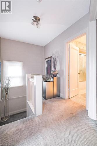 Light gray wall-to-wall carpeting, white painted stair railing, natural light from a window with blinds, and white trim throughout - 107 Bond Street S, Hamilton, ON - Indoor