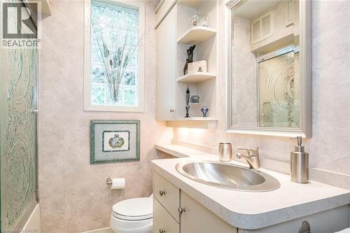 Vanity with integrated sink, built-in shelving, cabinet storage, and a glass block window - 107 Bond Street S, Hamilton, ON - Indoor Photo Showing Bathroom