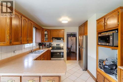 U-shaped kitchen featuring wood cabinetry, light countertops, and a white tile backsplash - 111 Decou Road, Simcoe, ON - Indoor Photo Showing Kitchen With Double Sink
