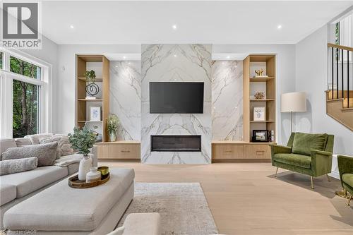Marble-look fireplace surround with an integrated linear electric fireplace, custom built-in shelving, wood-finish flooring, and recessed lighting - 67 Cielo Court, Hamilton, ON - Indoor Photo Showing Living Room With Fireplace