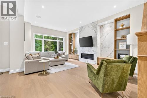 Spacious living area featuring expansive windows, wood-finish flooring, a wall-mounted fireplace, and built-in shelving - 67 Cielo Court, Hamilton, ON - Indoor Photo Showing Living Room With Fireplace
