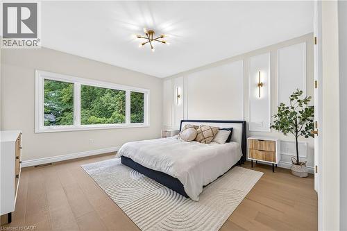 Expansive window providing abundant natural light, wood-finish flooring, accent wall paneling, and modern light fixtures - 67 Cielo Court, Hamilton, ON - Indoor Photo Showing Bedroom