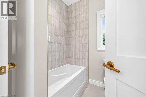 White bathtub with tiled surround featuring vertical rectangular tiles, and a window with white trim - 67 Cielo Court, Hamilton, ON - Indoor Photo Showing Bathroom