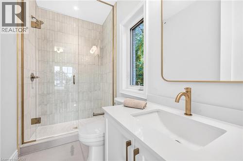 Walk-in shower with clear glass enclosure and gold-toned fixtures, rectangular wall-mounted mirror, single vanity with integrated sink, gold-toned faucet, and white countertop - 67 Cielo Court, Hamilton, ON - Indoor Photo Showing Bathroom