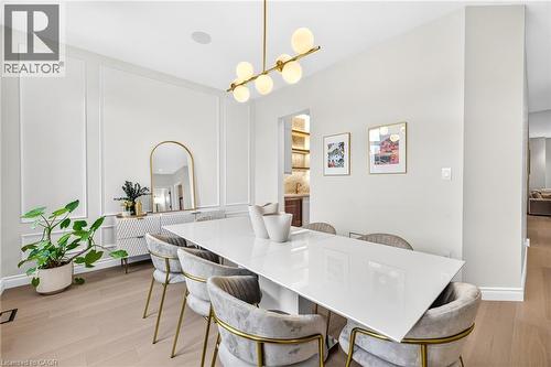 Light wood-finish flooring, architectural wall paneling, contemporary linear chandelier with frosted globes, recessed ceiling speakers, and crown molding - 67 Cielo Court, Hamilton, ON - Indoor Photo Showing Dining Room