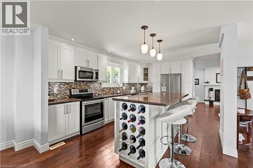 Kitchen featuring rich wood-finish flooring, white cabinetry, stainless steel appliances, a multi-tone tile backsplash, and an island with a built-in wine rack - 87 Monte Drive, Hamilton, ON - Indoor Photo Showing Kitchen With Stainless Steel Kitchen With Upgraded Kitchen