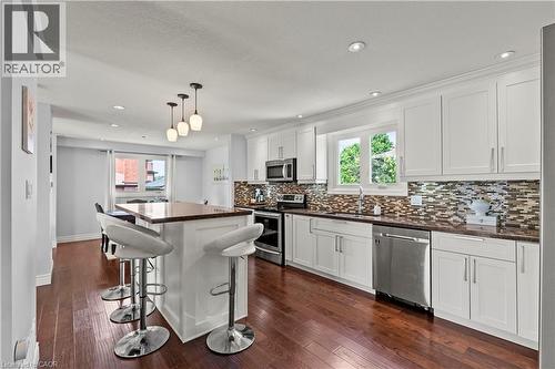 Kitchen featuring white cabinetry, stainless steel appliances, a mosaic tile backsplash, wood-finish flooring, and a central island with pendant lighting - 87 Monte Drive, Hamilton, ON - Indoor Photo Showing Kitchen With Stainless Steel Kitchen With Upgraded Kitchen