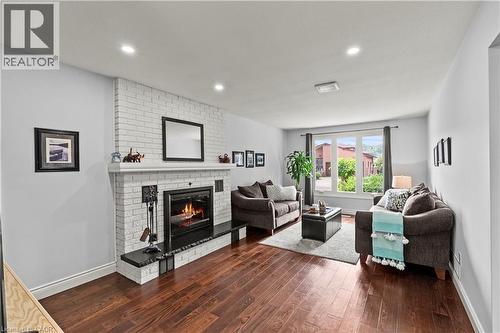 Living area featuring wood-finish flooring, a white brick fireplace with a dark hearth, and recessed ceiling lighting - 87 Monte Drive, Hamilton, ON - Indoor Photo Showing Living Room With Fireplace