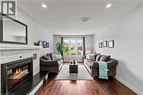 Recessed lighting, wood-finish flooring, white brick fireplace with dark hearth, and a large window - 87 Monte Drive, Hamilton, ON - Indoor Photo Showing Living Room With Fireplace