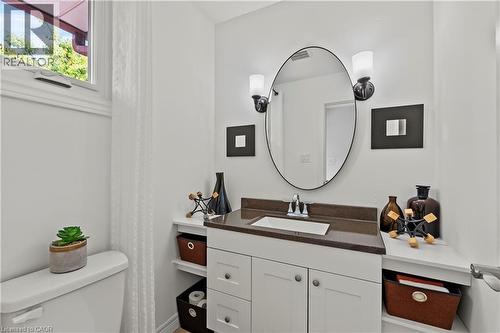 White vanity with a brown countertop, integral rectangular sink, oval mirror, and wall-mounted sconces - 87 Monte Drive, Hamilton, ON - Indoor Photo Showing Bathroom