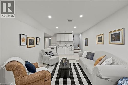 Recessed lighting illuminates the open living space, featuring a compact kitchen with white cabinetry, a built-in electric range, and a sink with a black faucet - 87 Monte Drive, Hamilton, ON - Indoor Photo Showing Living Room