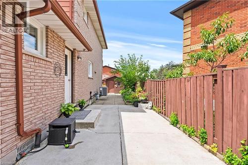 Brick exterior with brown downspouts, side concrete walkway, and a privacy fence - 87 Monte Drive, Hamilton, ON - Outdoor With Exterior