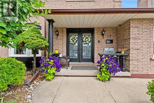 Brick exterior with a covered porch featuring black columns, double entry doors with decorative glass, and exterior lighting fixtures - 87 Monte Drive, Hamilton, ON - Outdoor With Deck Patio Veranda