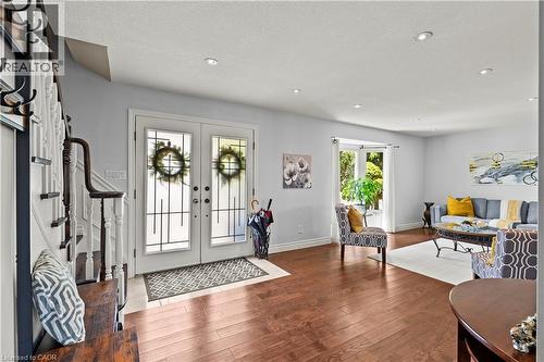 Wood-finish flooring throughout, white double entry doors with decorative glass panels, recessed ceiling lighting, and a white staircase with a dark wood handrail - 87 Monte Drive, Hamilton, ON - Indoor