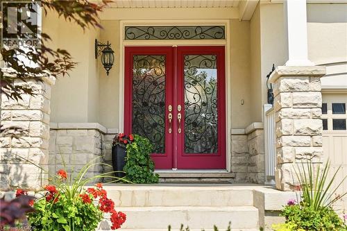 Elegant red double doors with decorative wrought-iron glass panels and transom window, flanked by stone pilasters and complemented by vibrant seasonal plantings and landscape beds - 536 Cusick Circle, Milton, ON - Indoor Photo Showing Other Room
