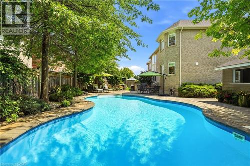 Sparkling resort-style swimming pool with curved design and crystal-clear water, surrounded by mature shade trees and lush landscaping - 536 Cusick Circle, Milton, ON - Outdoor With In Ground Pool With Backyard