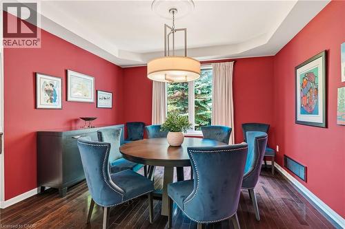 Sophisticated dining room showcasing vibrant coral walls, rich wood-finish flooring, and a round dining table anchored by a cylindrical pendant light fixture - 536 Cusick Circle, Milton, ON - Indoor Photo Showing Dining Room