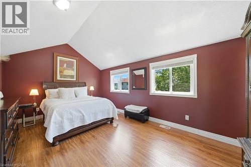 Vaulted ceiling with a flush-mount light fixture, two windows with white trim, wood-finish flooring, and a deep red accent wall - 784 Butternut Avenue, Waterloo, ON - Indoor Photo Showing Bedroom