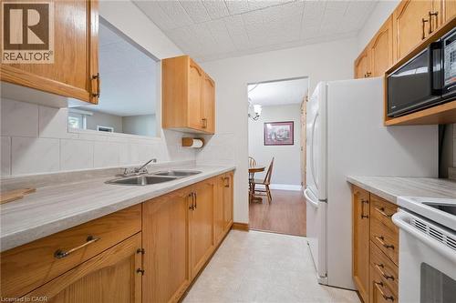 Kitchen featuring wood-finish cabinetry, a double basin stainless steel sink, and light-toned countertops - 6 Walton Avenue Unit# 107, Kitchener, ON - Indoor Photo Showing Kitchen With Double Sink