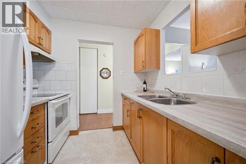 Kitchen featuring wood cabinetry, white appliances, a double basin stainless steel sink, and a white tile backsplash - 6 Walton Avenue Unit# 107, Kitchener, ON - Indoor Photo Showing Kitchen With Double Sink