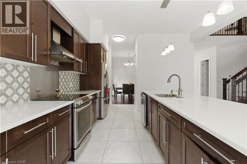 Chef's kitchen featuring rich wood cabinetry with stainless steel appliances, white quartz countertops, geometric tile backsplash, recessed and pendant lighting, and an oversized island with seating s - 2000 Maddex Way, London, ON - Indoor Photo Showing Kitchen With Double Sink With Upgraded Kitchen
