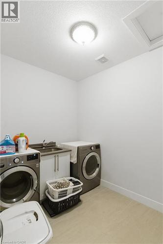 Dedicated laundry room featuring side-by-side front-load washers and dryers, ample counter space with cabinetry for storage, recessed ceiling lighting, and light wood-finish flooring throughout - 2000 Maddex Way, London, ON - Indoor Photo Showing Laundry Room