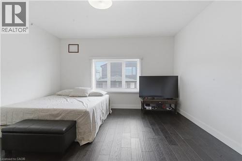 Bright bedroom offering dark wood-finish flooring, a bed with neutral linens, and a black storage bench - 2000 Maddex Way, London, ON - Indoor Photo Showing Bedroom