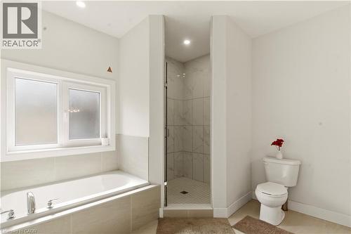 Modern primary bathroom featuring a soaking tub with tile surround, a corner walk-in shower with glass enclosure and tile walls, dual vanity sink, and wood-finish flooring - 2000 Maddex Way, London, ON - Indoor Photo Showing Bathroom