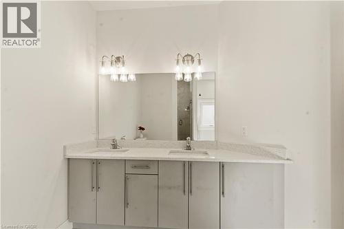 Modern bathroom vanity featuring dual sinks with a light stone countertop, ample cabinet storage with brushed metal hardware, and a large framed mirror illuminated by dual sconce lighting above - 2000 Maddex Way, London, ON - Indoor Photo Showing Bathroom