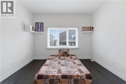 Bright bedroom featuring dark wood-finish flooring, white walls, and a large multi-pane window with horizontal blinds allowing abundant natural light - 2000 Maddex Way, London, ON - Indoor