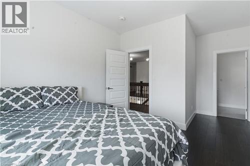 Spacious bedroom featuring dark wood-finish flooring, geometric patterned bedding, and abundant natural light from multiple windows - 2000 Maddex Way, London, ON - Indoor Photo Showing Bedroom