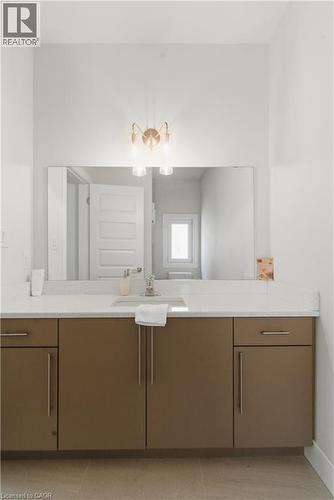 Spa-inspired bathroom vanity featuring warm wood-finish cabinetry with ample storage, a white quartz countertop, and an expansive framed mirror - 2000 Maddex Way, London, ON - Indoor