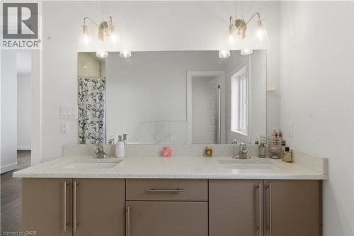 Dual-sink vanity featuring a white stone countertop, taupe cabinetry with polished nickel hardware, and an expansive mirror with integrated sconce lighting - 2000 Maddex Way, London, ON - Indoor Photo Showing Bathroom