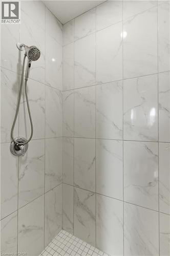 Spa-inspired shower featuring large-format marble-look tile walls with coordinating grout lines, dual showerheads with handheld spray attachment, chrome fixtures, and mosaic tile flooring - 2000 Maddex Way, London, ON - Indoor Photo Showing Bathroom