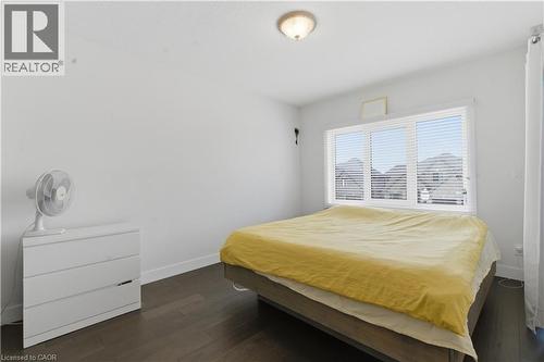 Dark wood-finish flooring, white walls, and a large window with horizontal blinds - 2000 Maddex Way, London, ON - Indoor Photo Showing Bedroom