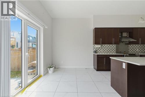 Modern kitchen featuring dark wood cabinetry with stainless steel hardware, a decorative tile backsplash, and a curved island with seating - 2000 Maddex Way, London, ON - Indoor Photo Showing Kitchen