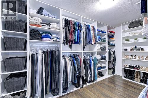 Custom walk-in closet featuring extensive built-in shelving, multiple hanging rods, dedicated shoe storage, wood-finish flooring, and recessed ceiling lighting - 1406 Marshall Crescent, Milton, ON - Indoor With Storage