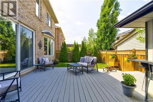 Spacious backyard featuring a gray composite deck, lush green lawn, mature evergreen trees, and a wooden privacy fence - 1406 Marshall Crescent, Milton, ON - Outdoor With Deck Patio Veranda With Exterior