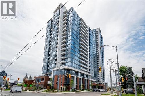 Modern high-rise building featuring extensive glass curtain walls, multiple balconies with glass railings, and a multi-story brick and glass base - 15 Wellington Street S Unit# 903, Kitchener, ON - Outdoor With Facade