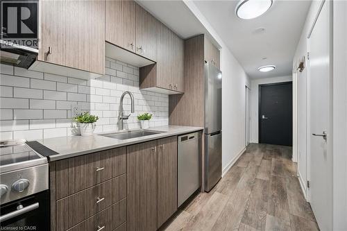 Kitchenette featuring stainless steel appliances, wood-finish cabinetry, light-toned countertop, and subway tile backsplash - 15 Wellington Street S Unit# 903, Kitchener, ON - Indoor Photo Showing Kitchen With Upgraded Kitchen