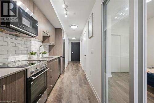 Galley kitchen featuring wood-finish cabinetry, stainless steel appliances, and a white subway tile backsplash - 15 Wellington Street S Unit# 903, Kitchener, ON - Indoor Photo Showing Kitchen With Upgraded Kitchen