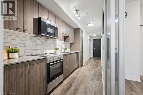 Contemporary kitchen featuring wood-finish cabinetry, stainless steel appliances, and a subway tile backsplash - 15 Wellington Street S Unit# 903, Kitchener, ON - Indoor Photo Showing Kitchen With Upgraded Kitchen