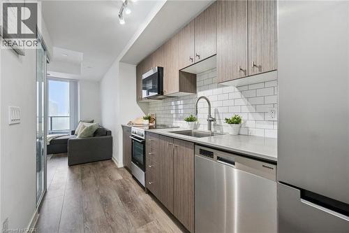 Modern kitchen featuring wood-finish cabinetry, stainless steel appliances, white subway tile backsplash, and light-toned countertops - 15 Wellington Street S Unit# 903, Kitchener, ON - Indoor Photo Showing Kitchen With Stainless Steel Kitchen With Upgraded Kitchen